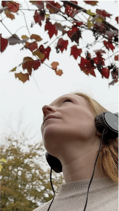 Woman with headphones looking up at leaves